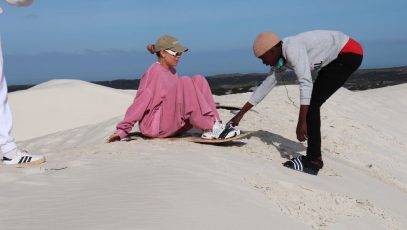 A woman being assisted whilst trying ultimate sandboarding at Wild X Adventures at the Atlantis Dunes