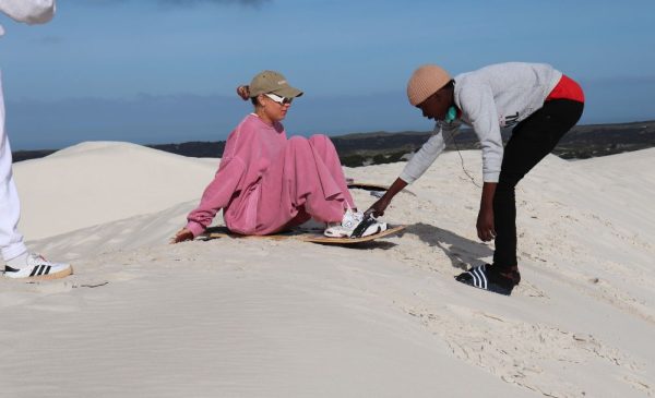 A woman being assisted whilst trying ultimate sandboarding at Wild X Adventures at the Atlantis Dunes