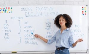 A stock photo of a woman in front of a white board teaching English